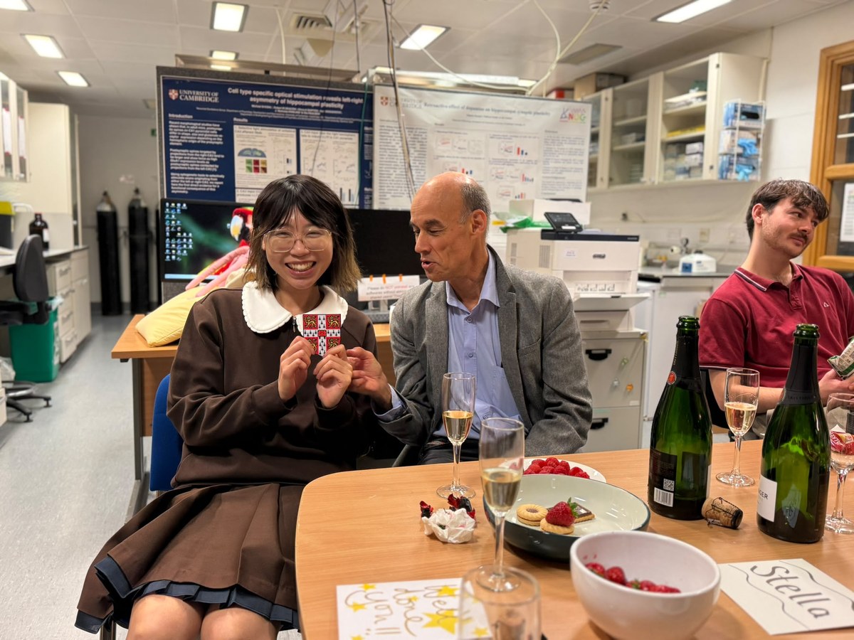 Stella Ma holding a University of Cambridge crest, celebrating with Ole Paulsen in the lab